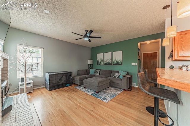 living room featuring ceiling fan, light hardwood / wood-style flooring, and a textured ceiling