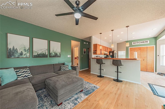 living room featuring ceiling fan, light hardwood / wood-style flooring, and a textured ceiling