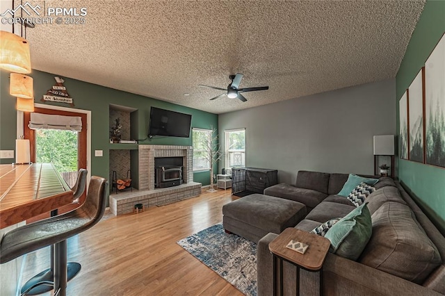 living room featuring a brick fireplace, hardwood / wood-style floors, a textured ceiling, and ceiling fan