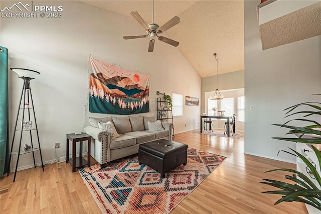 living room featuring ceiling fan, high vaulted ceiling, light hardwood / wood-style floors, and a textured ceiling