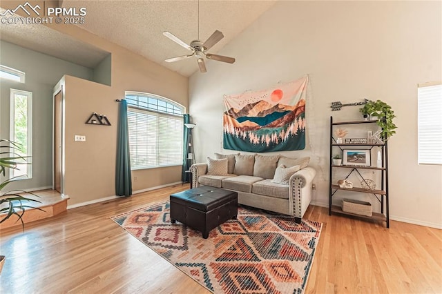 living room featuring ceiling fan, high vaulted ceiling, a textured ceiling, and light wood-type flooring