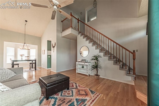 living room featuring ceiling fan with notable chandelier, wood-type flooring, high vaulted ceiling, and a textured ceiling