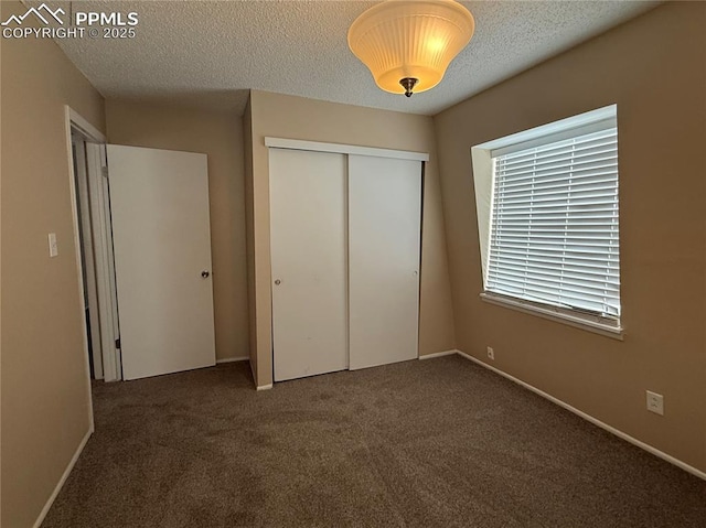 unfurnished bedroom with a textured ceiling, dark carpet, and a closet