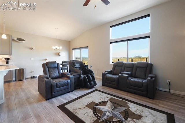 living room with ceiling fan with notable chandelier, high vaulted ceiling, and light hardwood / wood-style floors