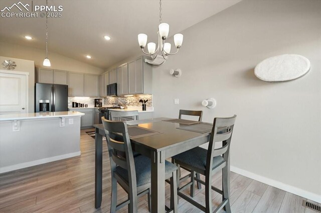 dining room featuring vaulted ceiling, an inviting chandelier, and light hardwood / wood-style floors