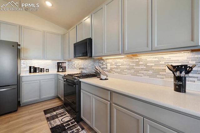 kitchen with stainless steel fridge, light hardwood / wood-style flooring, black gas range, tasteful backsplash, and vaulted ceiling