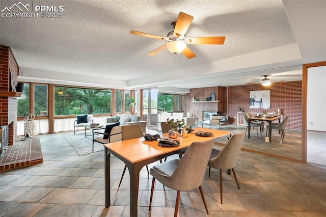 dining area with brick wall, a brick fireplace, a textured ceiling, and ceiling fan