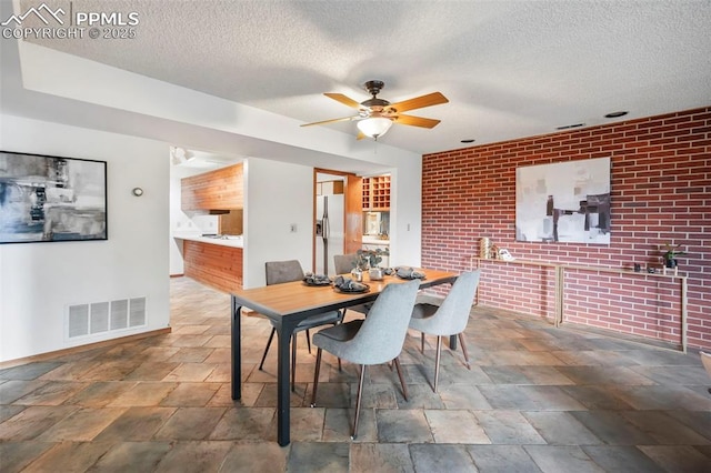 dining room with ceiling fan, brick wall, and a textured ceiling