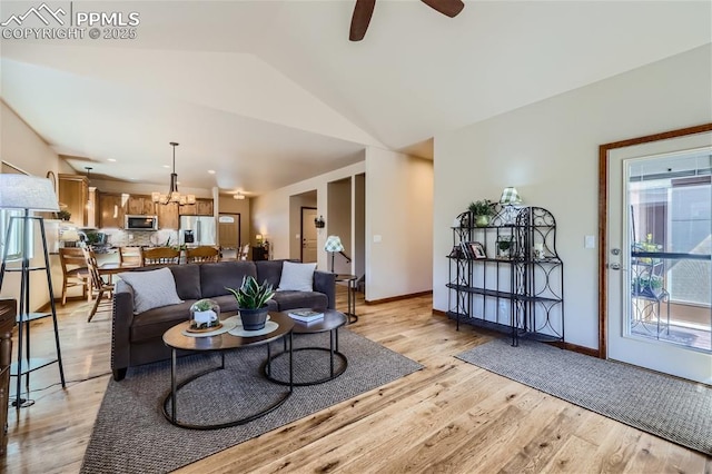 living room with ceiling fan with notable chandelier, vaulted ceiling, and light wood-type flooring