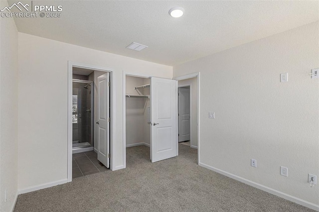 unfurnished bedroom with connected bathroom, carpet floors, a textured ceiling, a walk in closet, and a closet