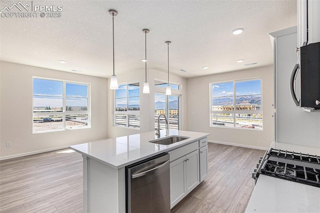 kitchen with pendant lighting, sink, white cabinetry, a kitchen island with sink, and stainless steel dishwasher