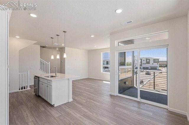 kitchen featuring pendant lighting, sink, dishwasher, light hardwood / wood-style floors, and a center island with sink