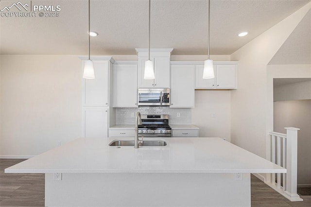 kitchen featuring stainless steel appliances, hanging light fixtures, a center island with sink, and decorative backsplash