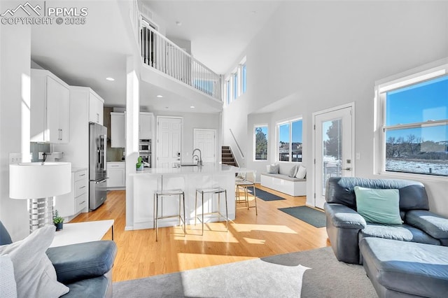 living room with sink, a towering ceiling, and light wood-type flooring