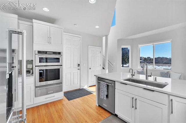 kitchen featuring stainless steel appliances, white cabinetry, sink, and light hardwood / wood-style flooring