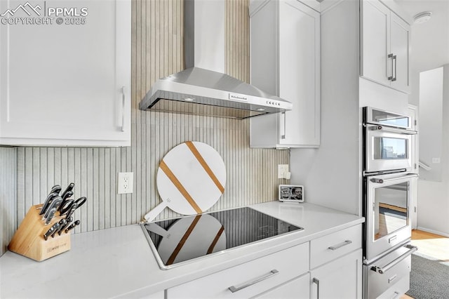 kitchen featuring white cabinetry, wall chimney range hood, double oven, and black electric stovetop