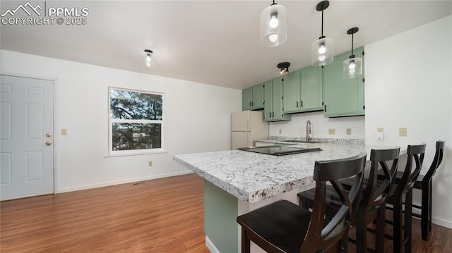 kitchen with sink, green cabinets, white refrigerator, a kitchen bar, and kitchen peninsula