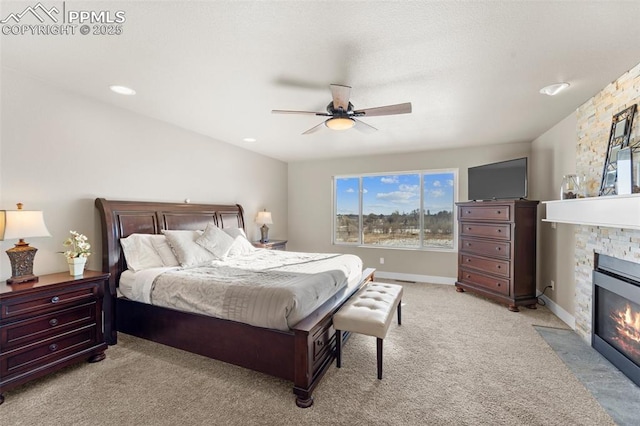 bedroom featuring a stone fireplace, light colored carpet, and ceiling fan