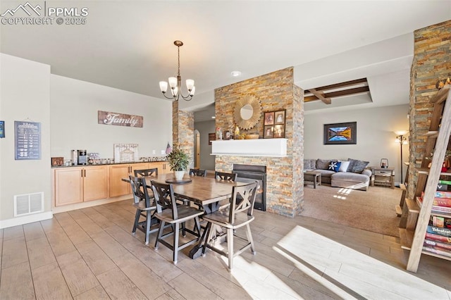 dining room with a notable chandelier, a stone fireplace, beamed ceiling, and light wood-type flooring