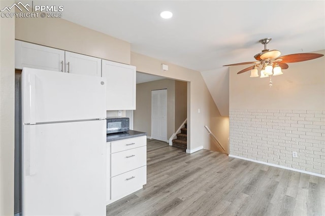 kitchen featuring ceiling fan, white refrigerator, white cabinets, vaulted ceiling, and light wood-type flooring