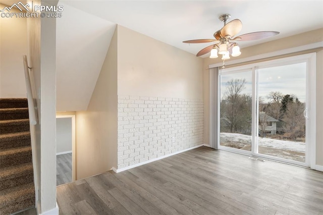 interior space featuring ceiling fan, brick wall, and hardwood / wood-style floors