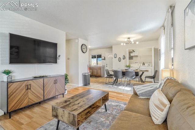 living room featuring an inviting chandelier, washer and clothes dryer, sink, and light hardwood / wood-style flooring