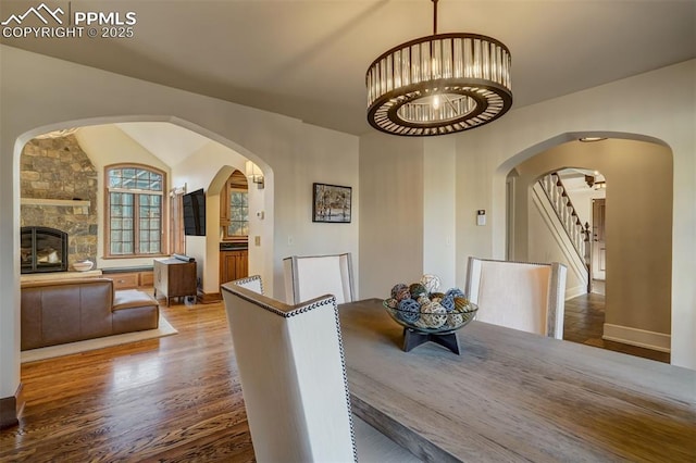 dining room featuring stairs, a fireplace, wood finished floors, and lofted ceiling