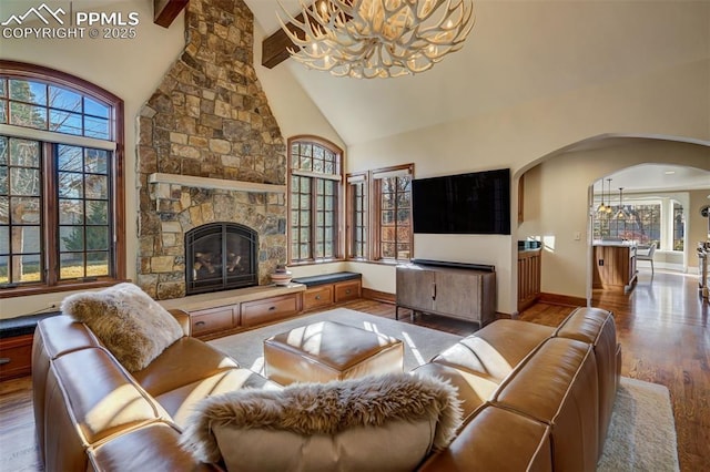 living area with high vaulted ceiling, a fireplace, wood finished floors, a healthy amount of sunlight, and an inviting chandelier