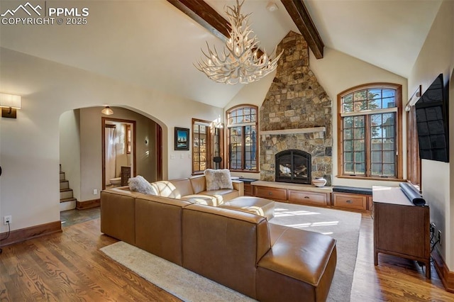 living area featuring arched walkways, high vaulted ceiling, a stone fireplace, wood finished floors, and beam ceiling