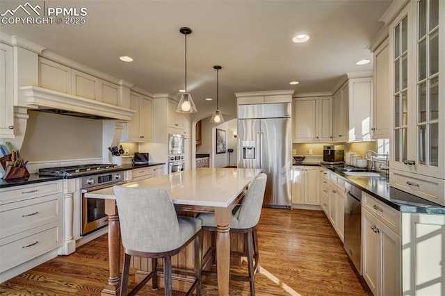 kitchen with dark countertops, glass insert cabinets, a center island, built in appliances, and a sink