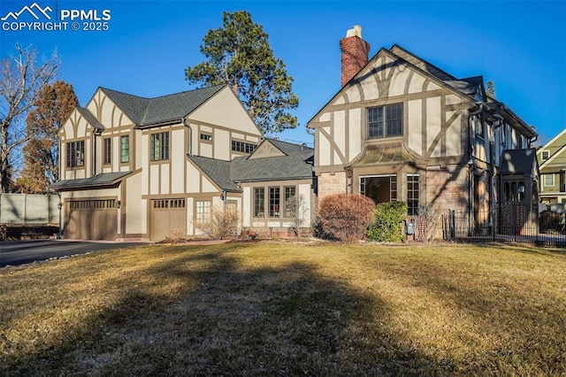 tudor home with aphalt driveway, a chimney, an attached garage, and stucco siding