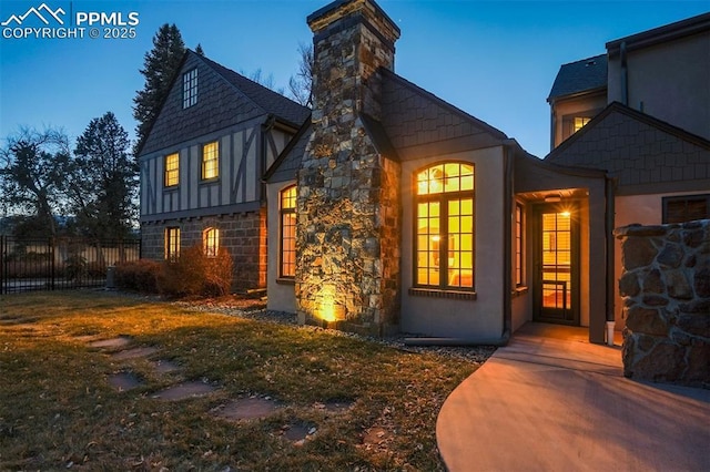 back of property at dusk with stone siding, fence, a chimney, and stucco siding