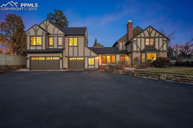 english style home featuring driveway, a chimney, an attached garage, and stucco siding