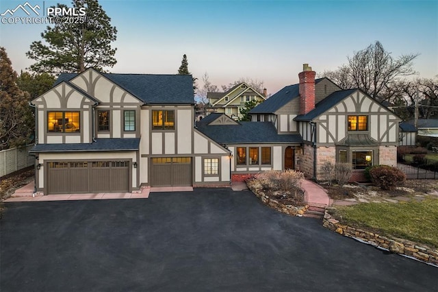 english style home featuring aphalt driveway, a chimney, an attached garage, and stucco siding