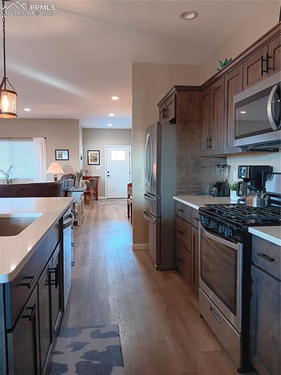 kitchen featuring dark brown cabinetry, sink, appliances with stainless steel finishes, dark hardwood / wood-style floors, and pendant lighting