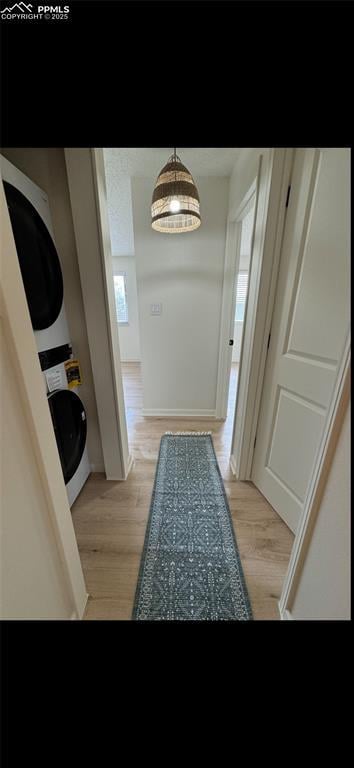 corridor with stacked washer / drying machine and light hardwood / wood-style flooring