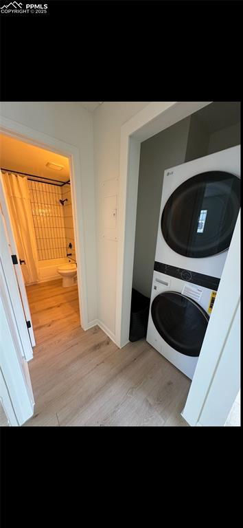 laundry room with stacked washing maching and dryer and light hardwood / wood-style flooring