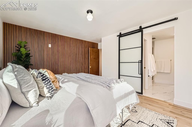 bedroom with a barn door, wooden walls, and light hardwood / wood-style flooring