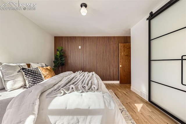 bedroom with a barn door, wooden walls, and light hardwood / wood-style floors