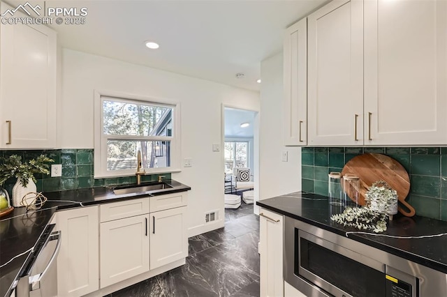 kitchen with stainless steel microwave, sink, white cabinetry, and backsplash