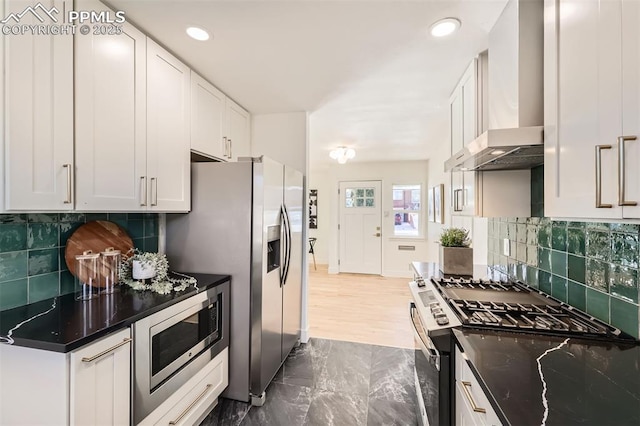 kitchen with white cabinets, decorative backsplash, stainless steel appliances, and wall chimney exhaust hood