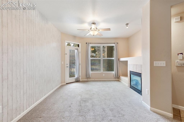 unfurnished living room with a tile fireplace, light colored carpet, and ceiling fan