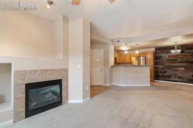 unfurnished living room with ceiling fan, light colored carpet, a tiled fireplace, and wood walls