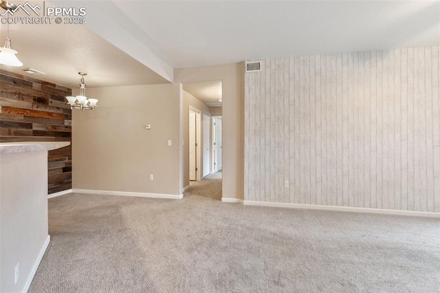 spare room with carpet floors, a chandelier, and wood walls