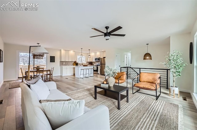 living room with ceiling fan, electric panel, and light wood-type flooring