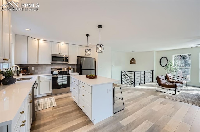 kitchen with pendant lighting, sink, stainless steel appliances, a center island, and white cabinets