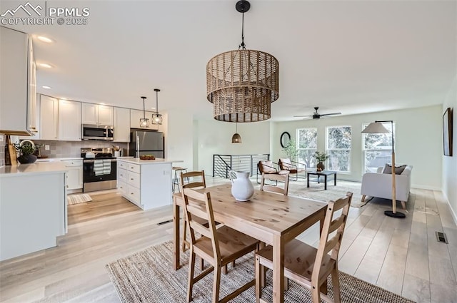 dining room with ceiling fan with notable chandelier and light hardwood / wood-style floors