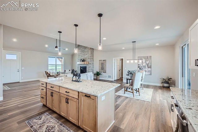 kitchen featuring pendant lighting, a fireplace, light brown cabinetry, a center island, and light stone countertops