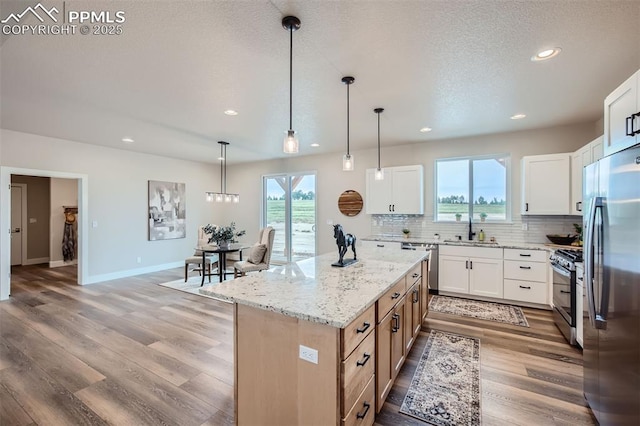 kitchen featuring light stone counters, decorative light fixtures, a kitchen island, stainless steel appliances, and white cabinets