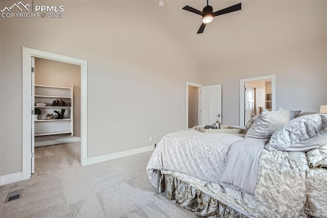 carpeted bedroom with ensuite bath, a walk in closet, high vaulted ceiling, and ceiling fan